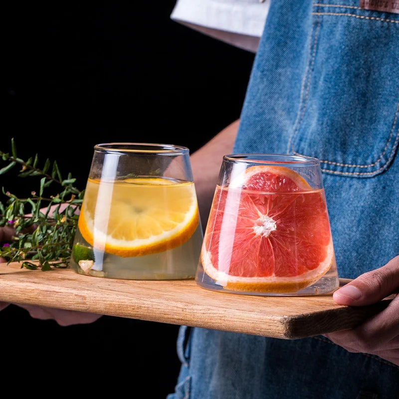 Two glasses of fruit-infused drinks on a wooden tray held by a person wearing blue jeans.