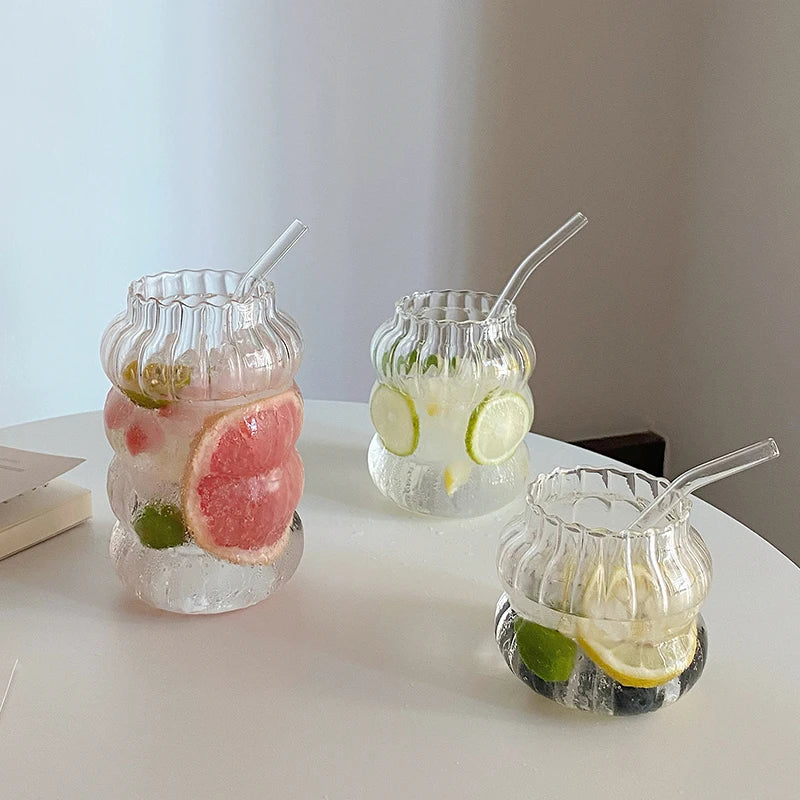 Three glass jars with decorative lids, each containing a drink with fruit slices and straws on a white surface.