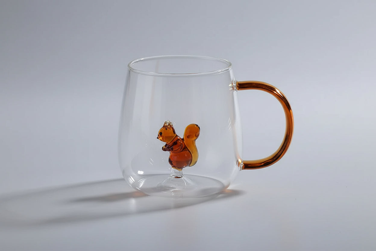 Clear glass mug with a brown handle and a small brown squirrel figure on a white surface.