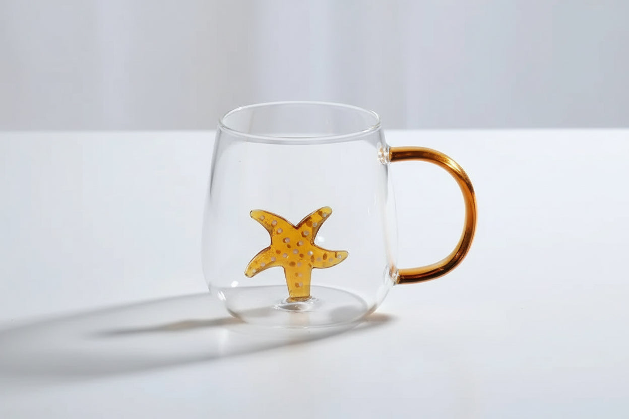Clear glass mug with a gold handle and starfish design on a white surface