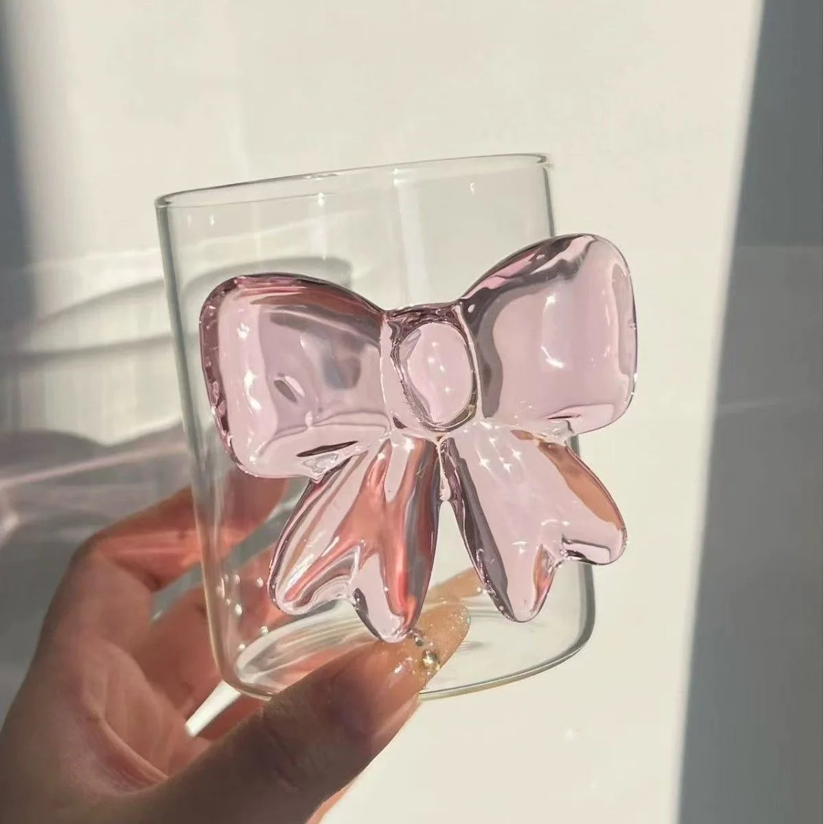 Clear glass with a pink bow decoration held by a hand against a neutral background