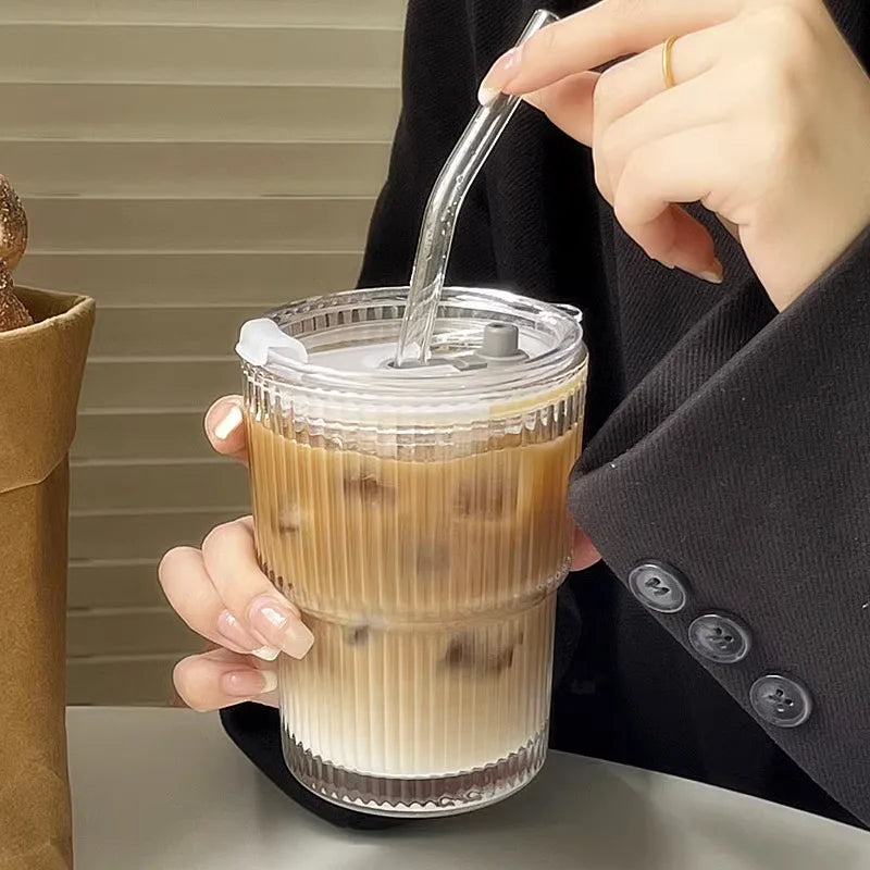 Person stirring iced coffee with a straw in a clear glass.