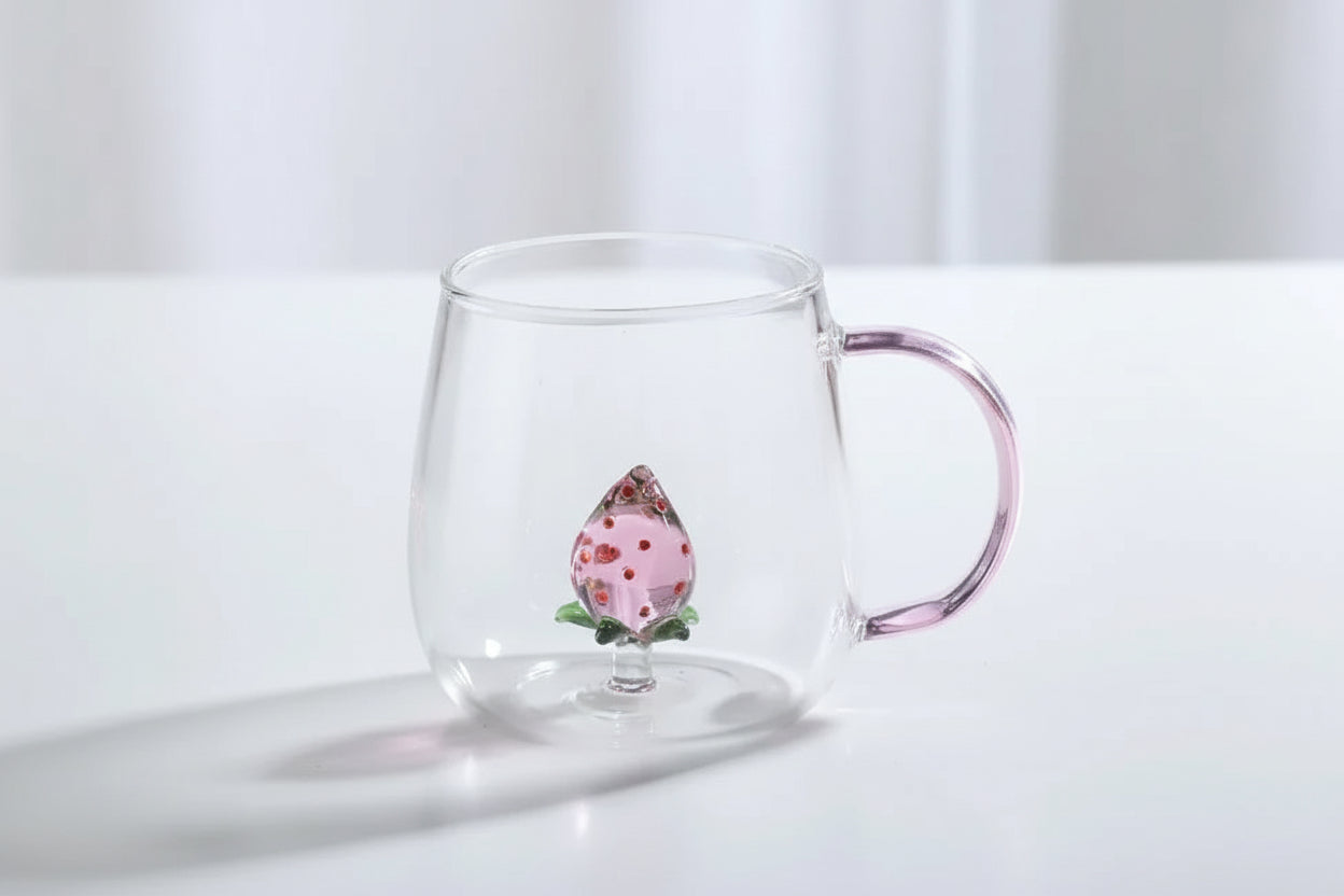 Clear glass mug with pink handle and strawberry decoration on a white surface