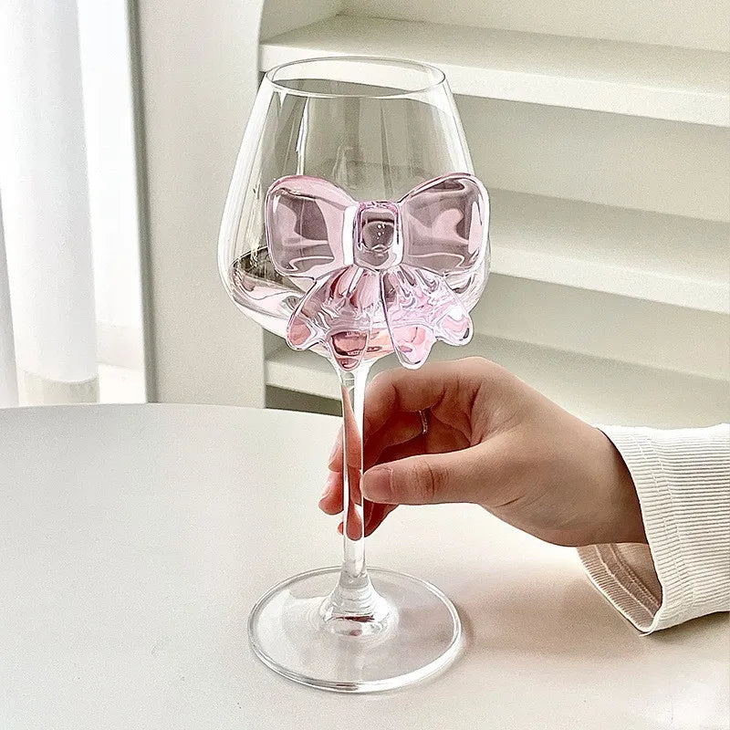 Clear wine glass with a pink bow held by a hand on a light background