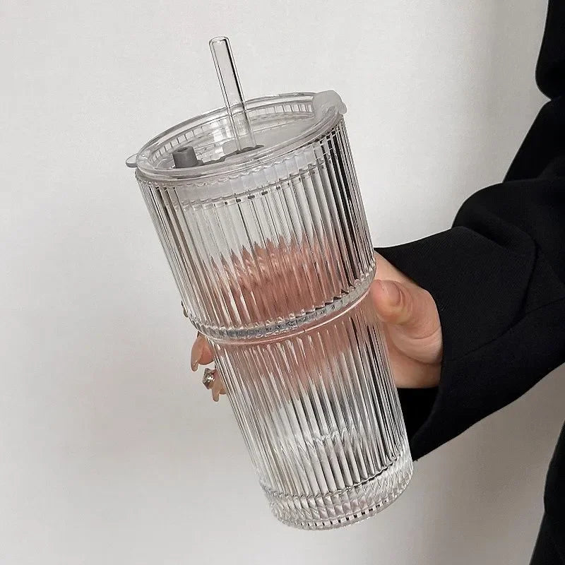 Clear ribbed tumbler with a straw held by a person against a plain background