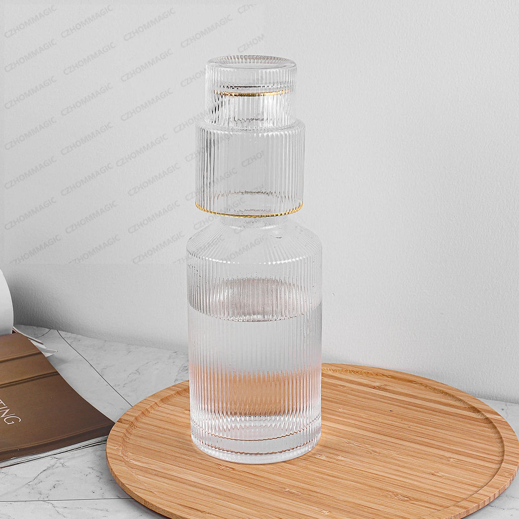 Clear glass carafe with ribbed design on a wooden coaster against a light background