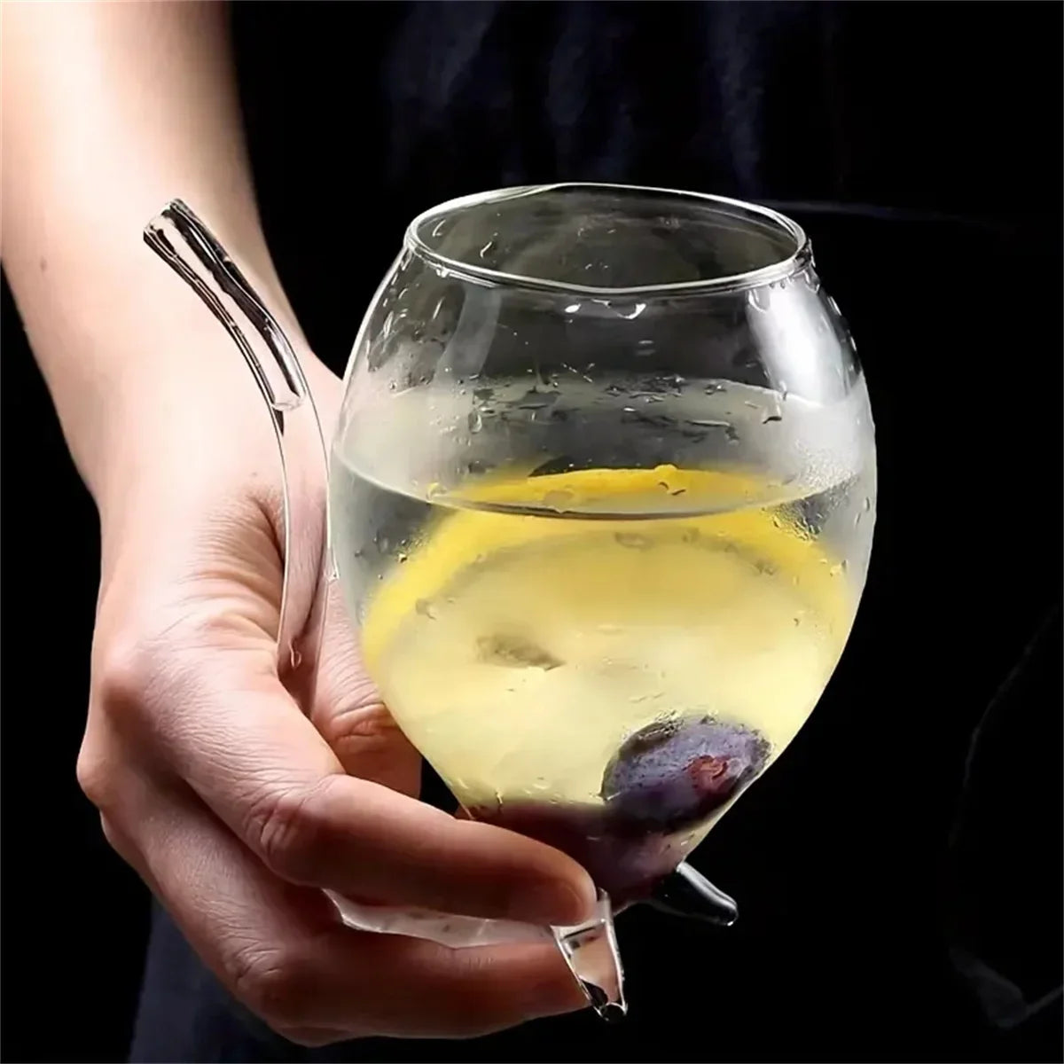 Hand holding a glass of lemonade with ice cubes against a black background
