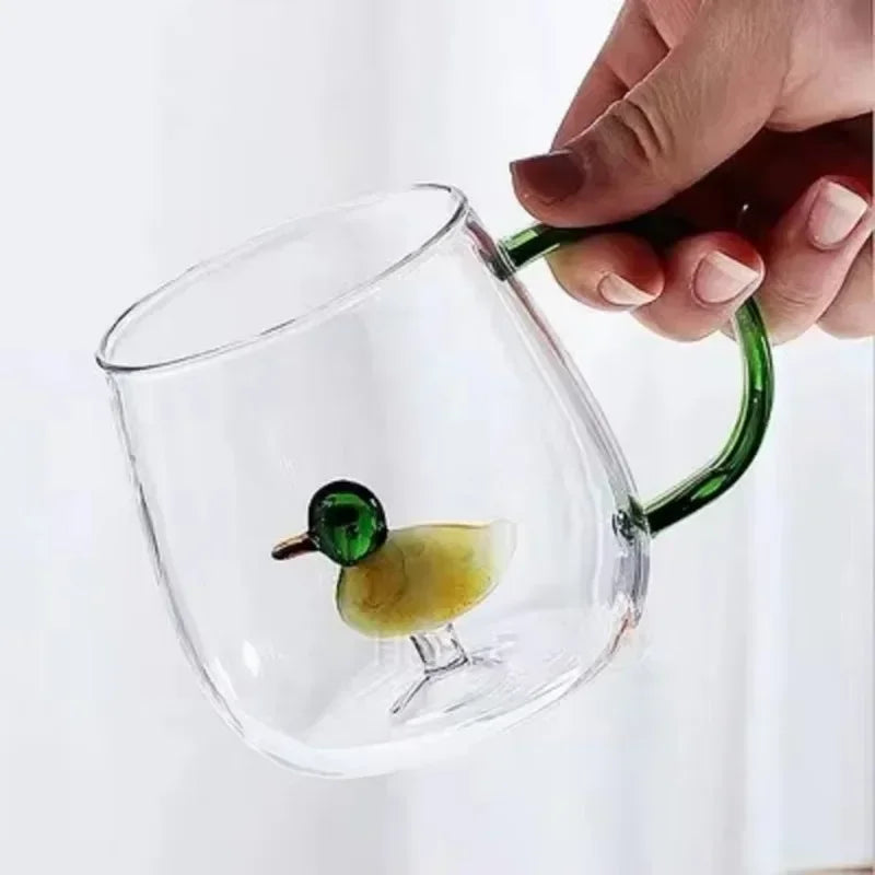 Clear glass mug with a green duck design held by a hand on a white background