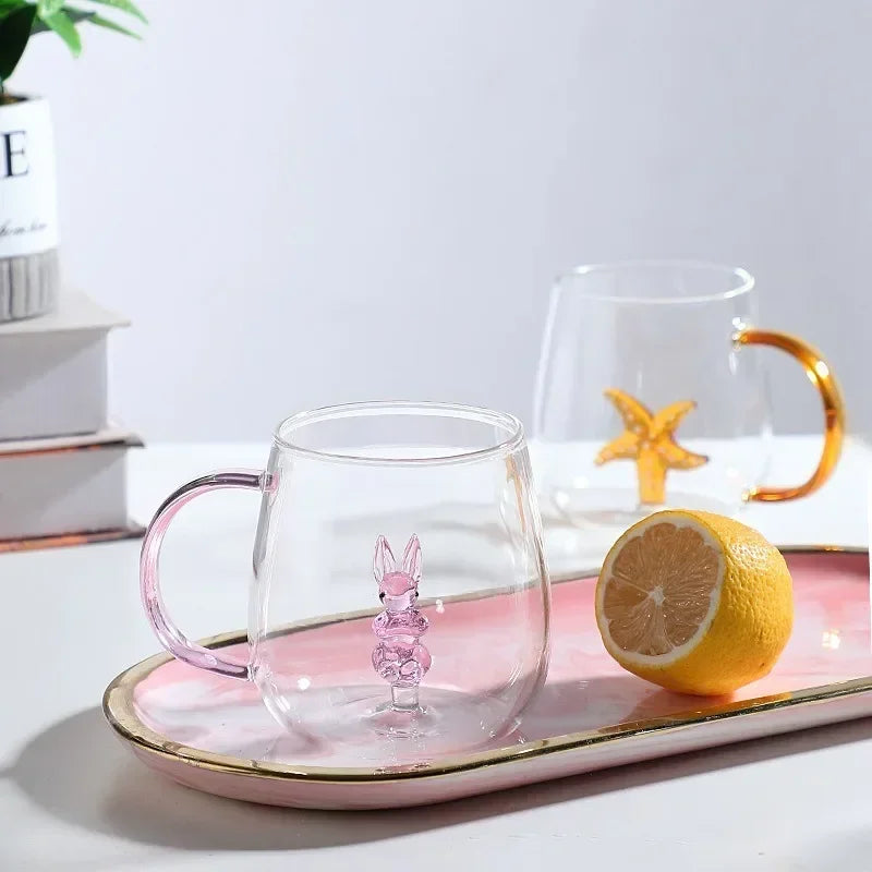Clear glass mug with pink rabbit design on a pink tray with a lemon, on a light gray background.