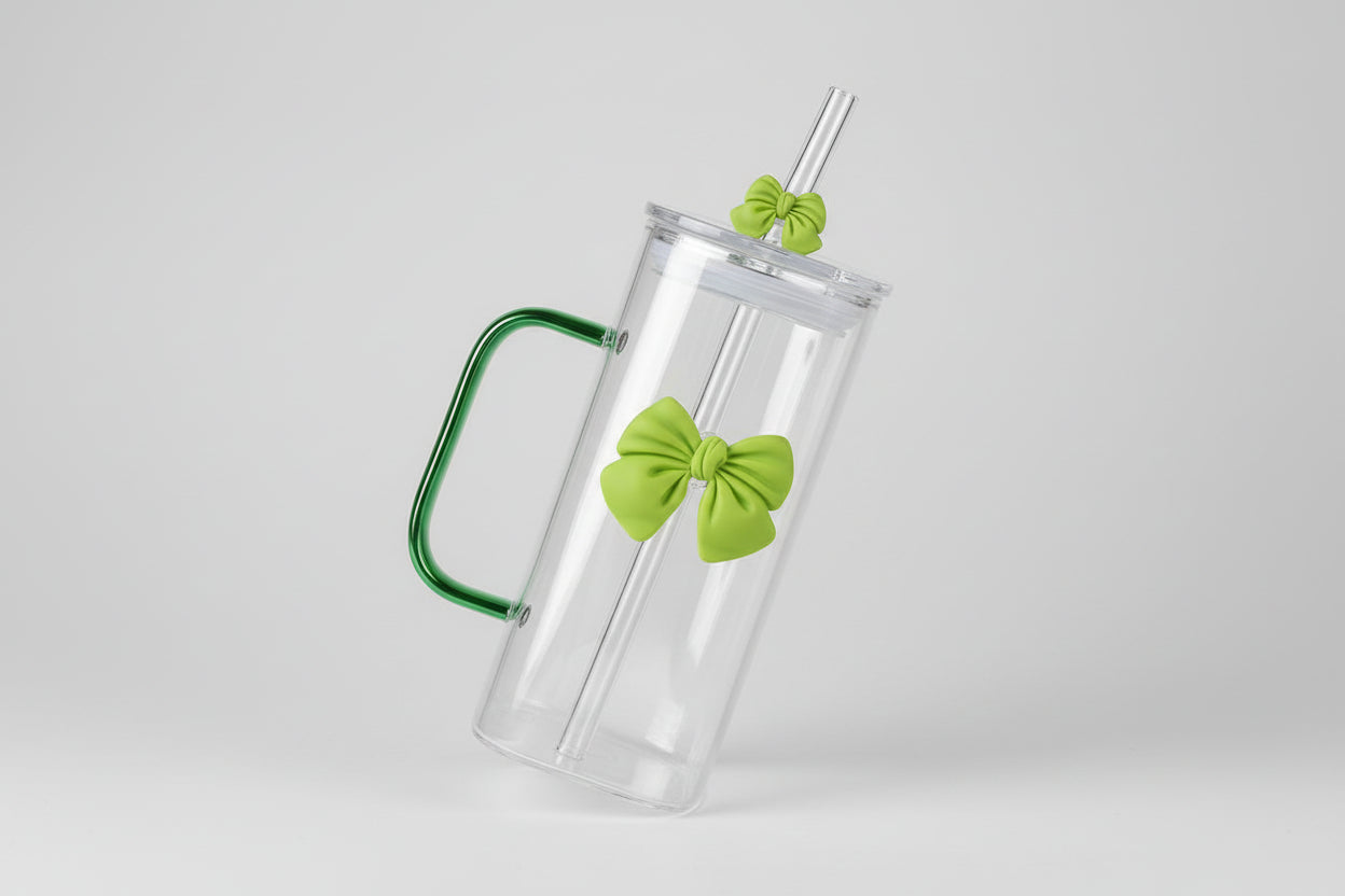Clear glass mug with green handles and bow accents held by a hand.