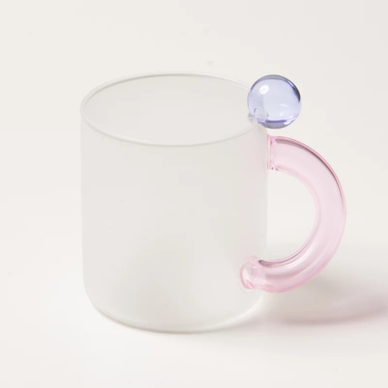 Clear glass mug with a pink handle and a small purple gem on a white background