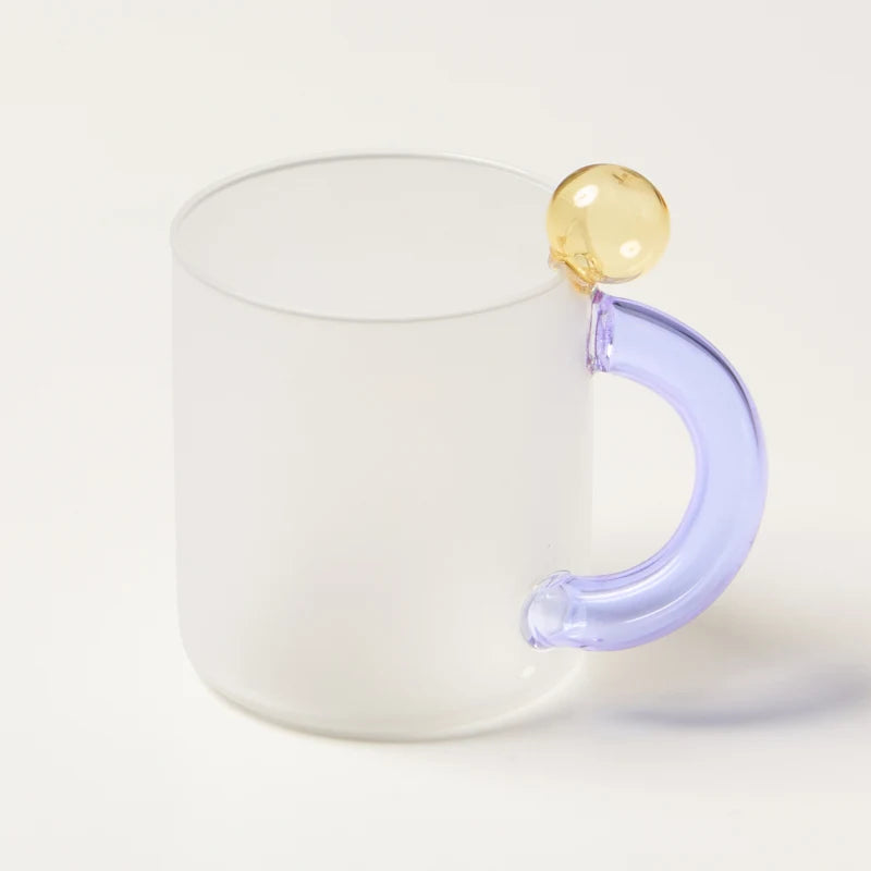 White mug with a unique handle featuring a yellow sphere and purple curved design on a white background