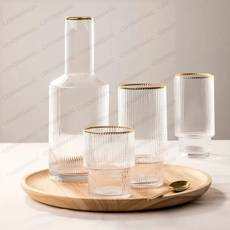 Clear glass carafe and tumblers with gold rims on a wooden tray.