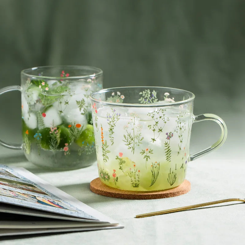 Two transparent mugs with floral designs on a light surface with a blurred green background