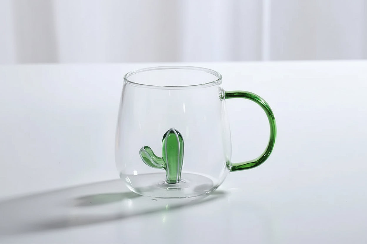 Clear glass mug with green handle and cactus design on a white surface
