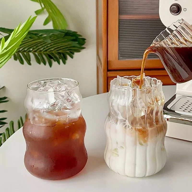 Iced coffee being poured into a glass with ice and a milk-based drink on a table.
