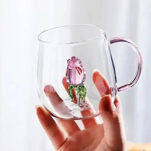 Clear glass mug with pink tulip design held by a hand against a white background