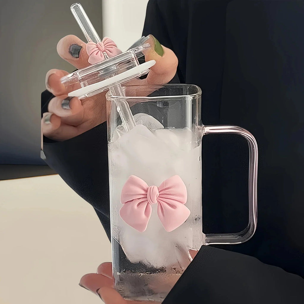 Clear mug with pink bow and straw, held by a person.