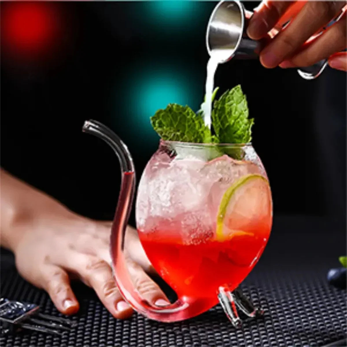 Red cocktail with mint leaves being poured into a glass held by a hand.
