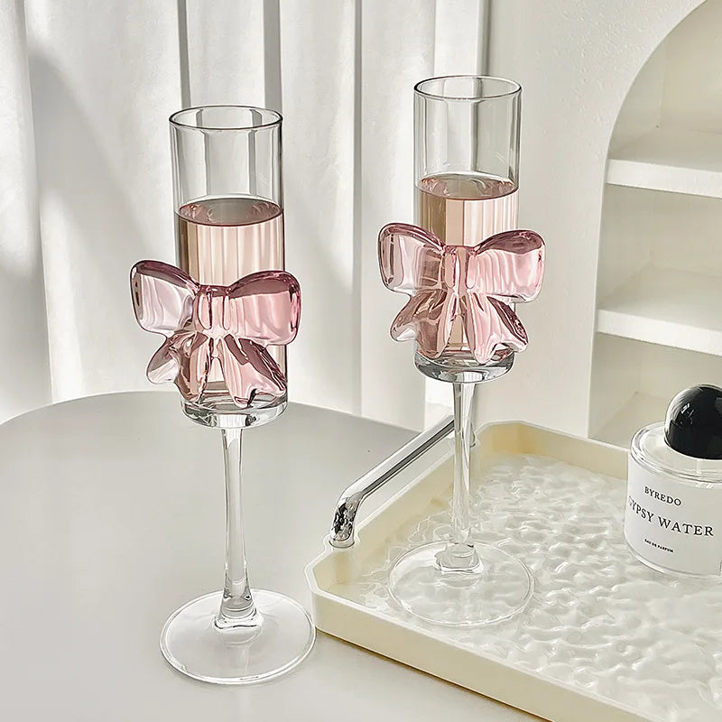 Two champagne flutes with pink bow decorations on a white surface.