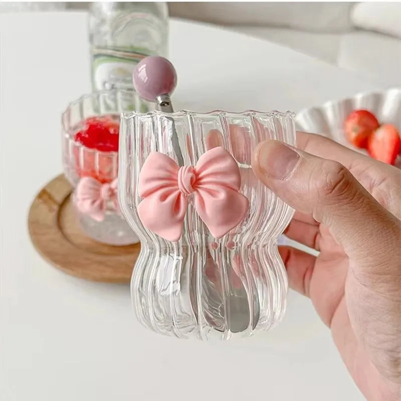 Clear glass with pink bow and cherry design held by a hand on a light background