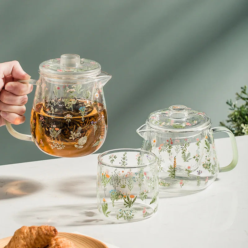 Glass teapot and mug with floral designs on a light surface.