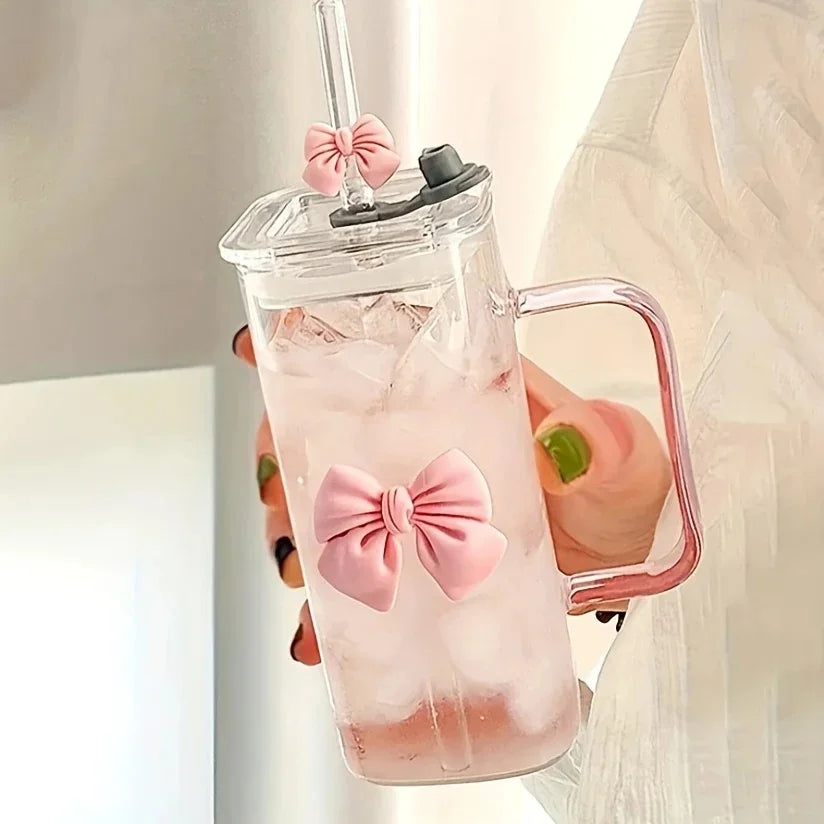 Clear tumbler with pink bow design, handle, and straw lid held by a person.