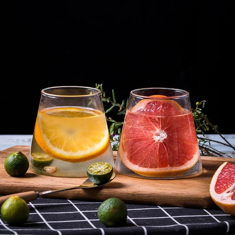 Two glasses of fruit-infused drinks on a wooden cutting board with limes and a dark background.