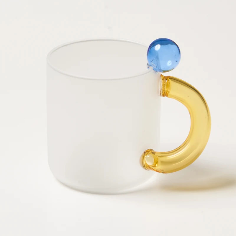 White mug with a gold handle and blue bead on a white background